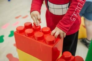 Kind speelt met grote rode Legoblok tijdens activiteit.