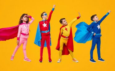 Kinderen in kleurrijke superheldenkostuums met capes op gele achtergrond.