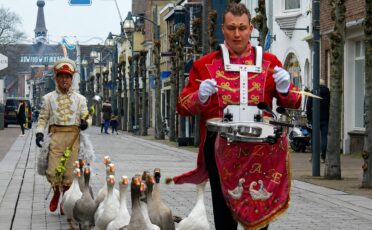 Clown Snoepy leidt een parade met zwanen in een straat.