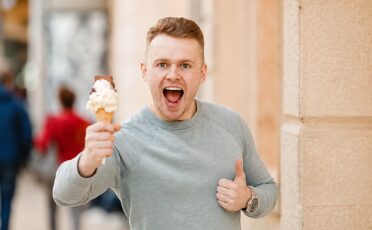 Man met ijsje in hand, lachend en blij op straat.